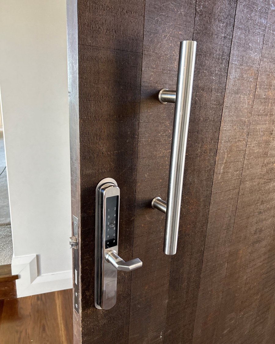 Stainless slimline smart lock beside a tall pull handle on a dark stained timber door