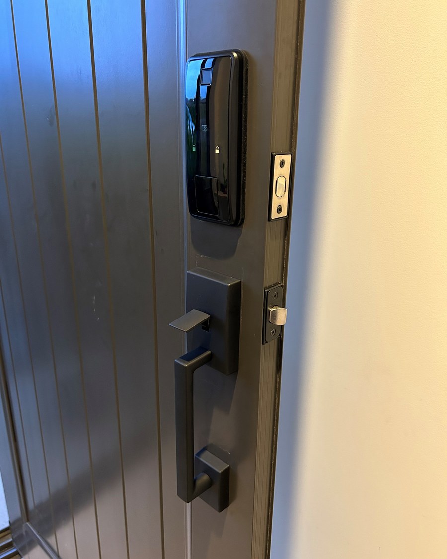 Black smart deadbolt above a grip handleset on a dark timber entrance door