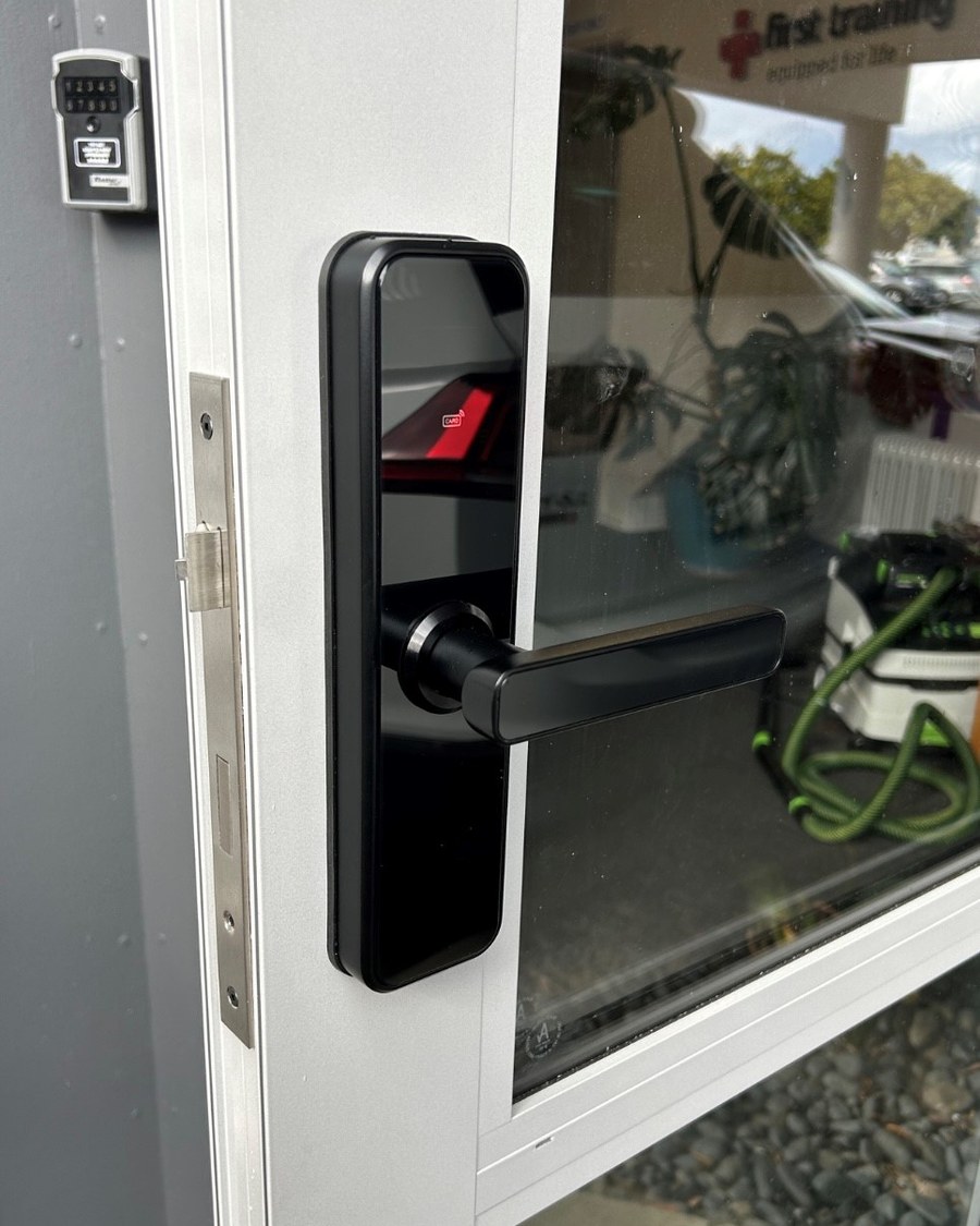 Black smart lock on a white aluminium commercial glazed door, with a key safe alongside
