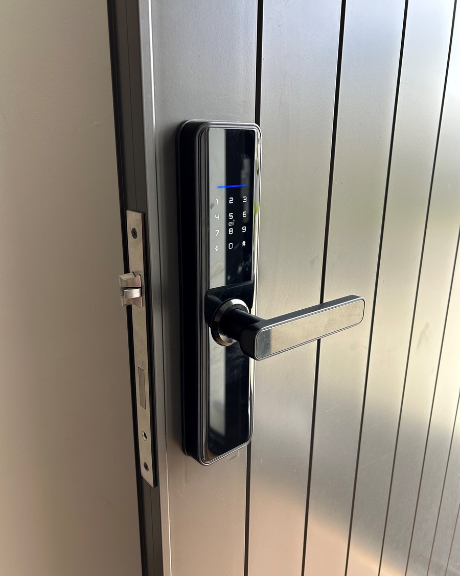 Black smart lock with a lit status strip on a grey grooved metal faced door